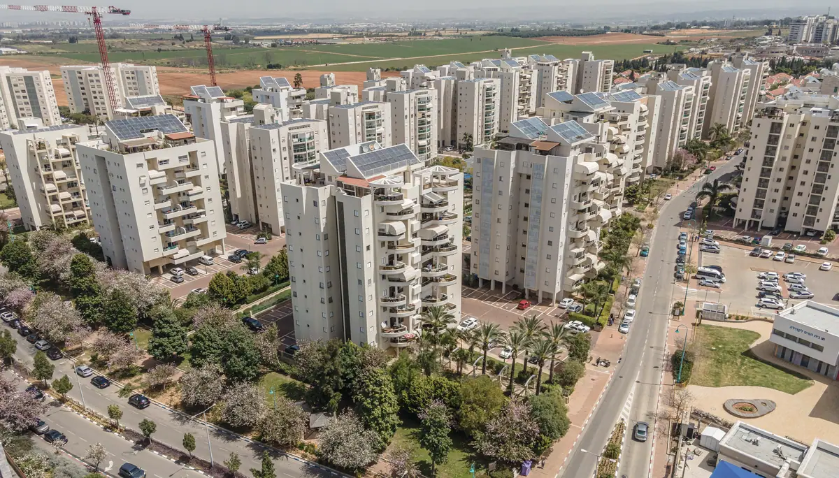 בנייני מגורים בשכונה בישראל ממבט אווירי: הבניינים עם המגרשים, החניות והגינות המשותפות לצד הרחוב.